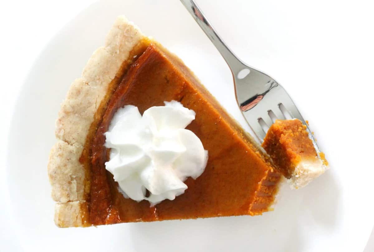 A slice of pumpkin pie with a bite out and a fork.