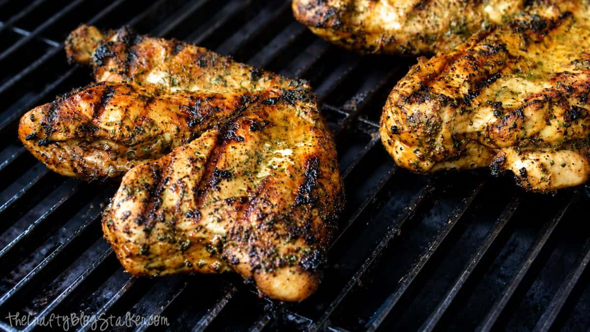 Grilled cilantro lime chicken breasts cooking on black grill grates with char marks and fresh herb seasoning.