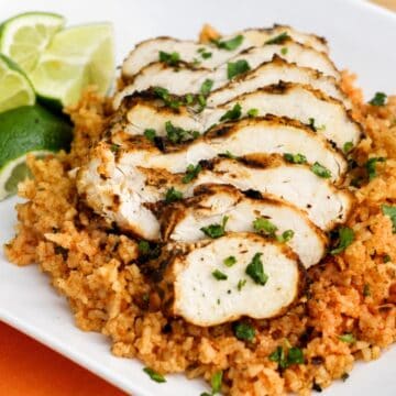 Sliced grilled chicken over cilantro lime rice with fresh lime wedges and chopped cilantro on a white dinner plate.