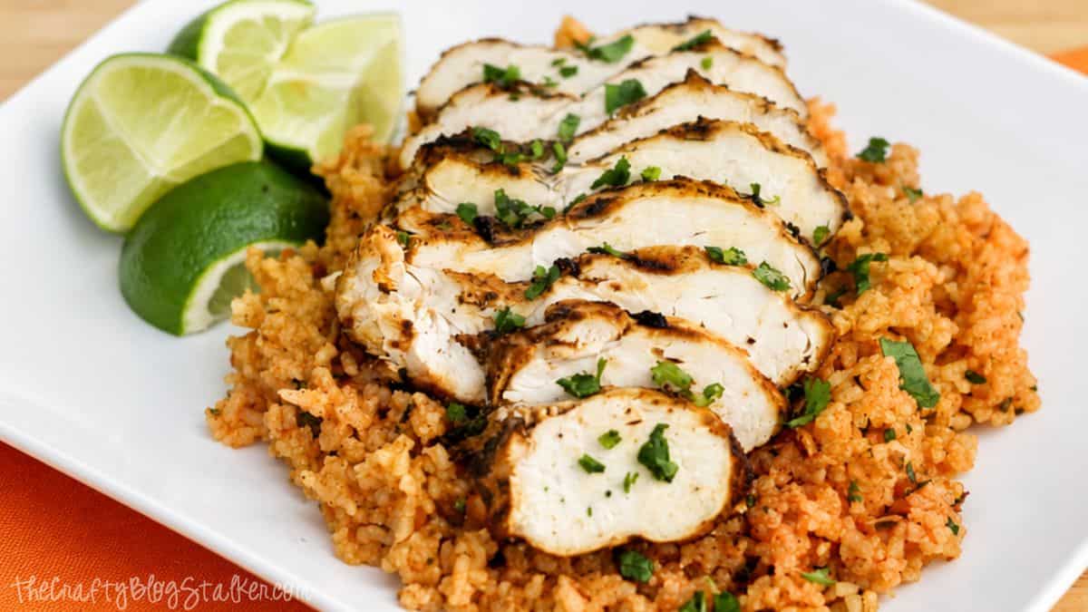 This Cilantro Lime Grilled Chicken is one of the easiest and most delicious ways to prepare grilled chicken. Sliced grilled chicken over cilantro lime rice with fresh lime wedges and chopped cilantro on a white dinner plate.