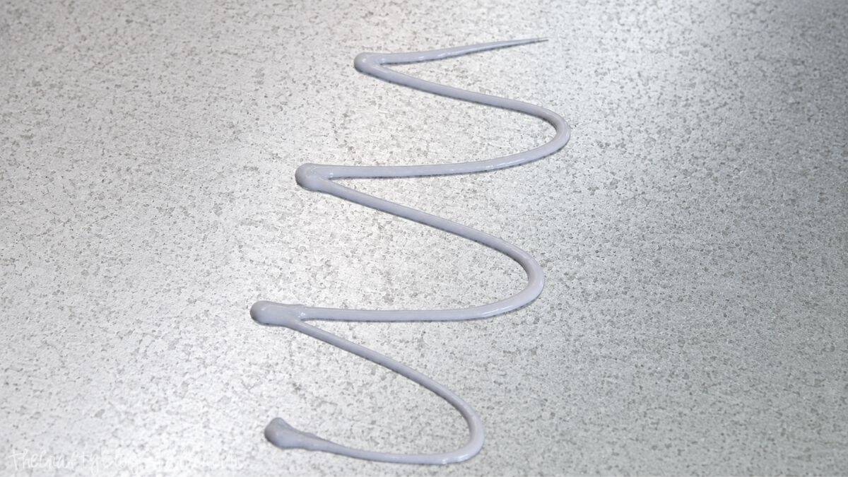 Zigzag bead of construction adhesive applied to galvanized sheet metal before installing it inside a medicine cabinet.