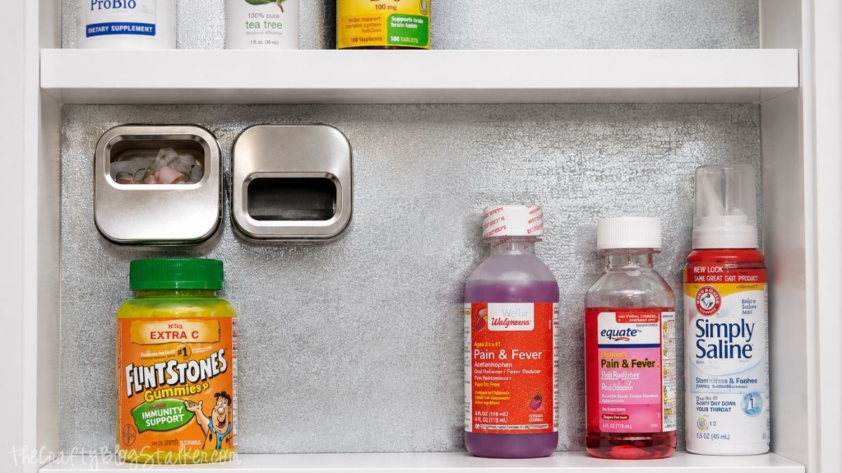 Magnetic medicine cabinet with a handwritten note, scissors on a magnetic hook, and organized vitamins and essential oils on the shelf.