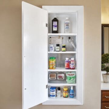 Open wall-mounted medicine cabinet with organized shelves, magnetic storage containers, vitamins, and medications beside a bathroom vanity.