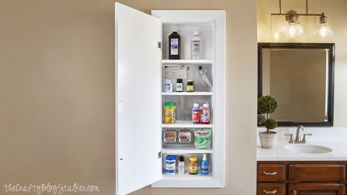 Open wall-mounted medicine cabinet with organized shelves, magnetic storage containers, vitamins, and medications beside a bathroom vanity.
