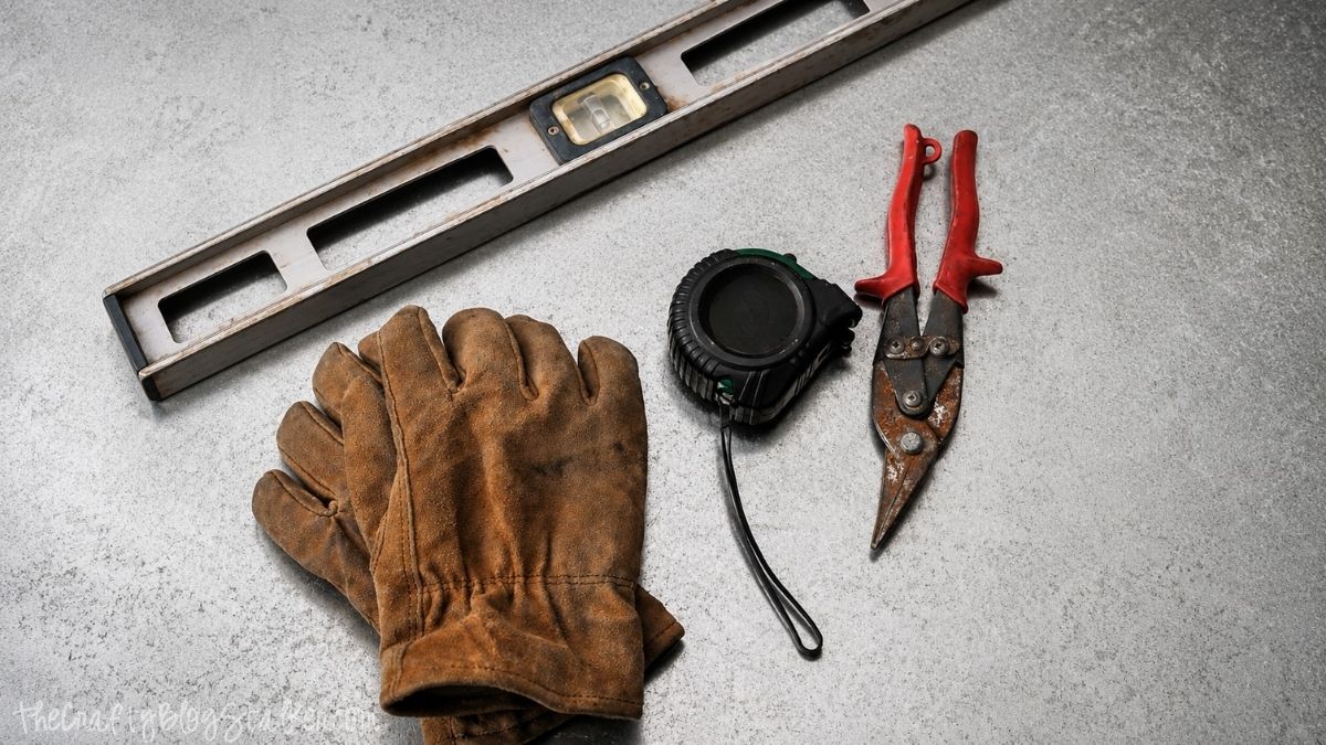 Level, leather work gloves, tape measure, and metal snips arranged on a workbench, showing basic tools for a home improvement project.