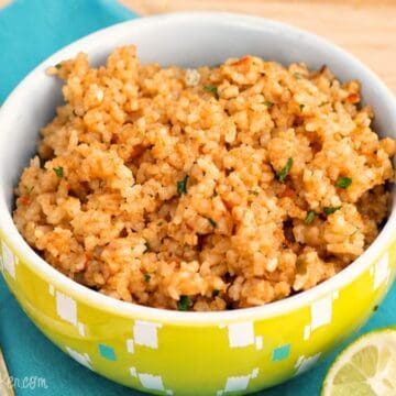 Bowl of Mexican rice on a teal napkin with a fork and lime wedges on a wooden table.