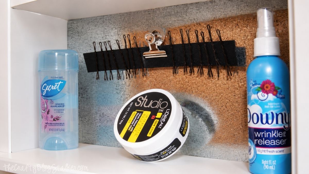 Magnetic medicine cabinet shelf with bobby pins on a magnetic strip, deodorant, hair styling paste, wrinkle release spray, and a cork organizer.