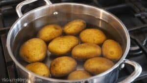 Yellow potatoes boiling in a stainless steel pot of water on the stovetop before being smashed and baked for BBQ chicken smashed potatoes.