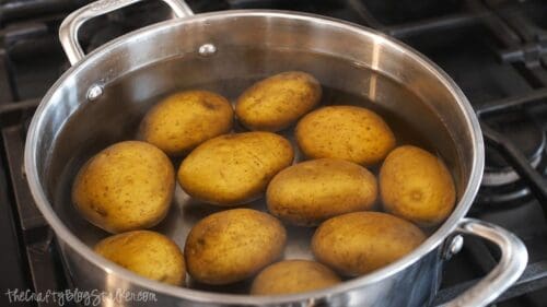 Yellow potatoes boiling in a stainless steel pot of water on the stovetop before being smashed and baked for BBQ chicken smashed potatoes.