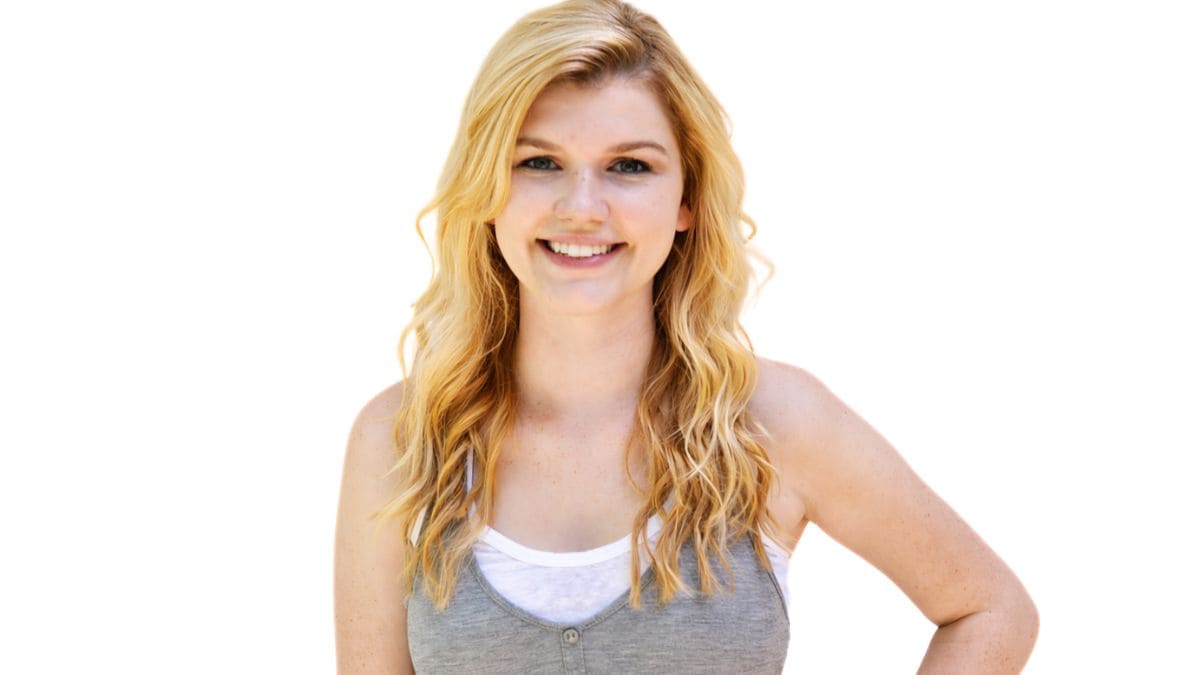 Smiling woman with long wavy hair, wearing a tank top, facing forward with one hand on her hip.