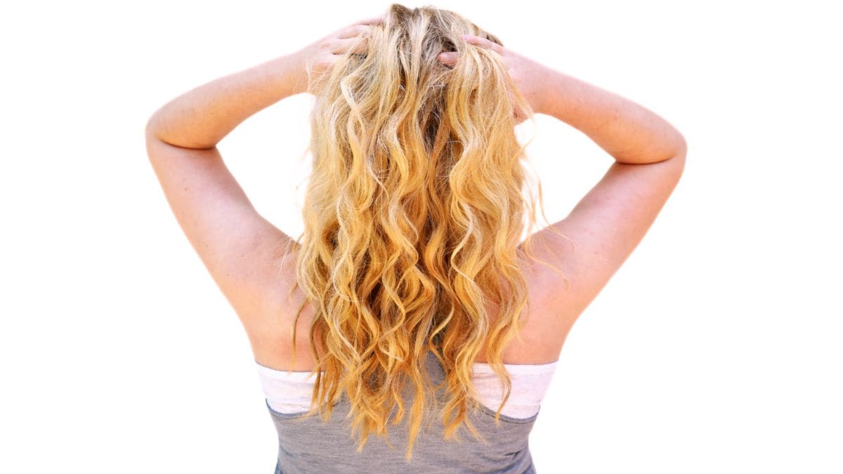 Back view of a woman with long wavy hair, arms raised and hands holding the top of her head.