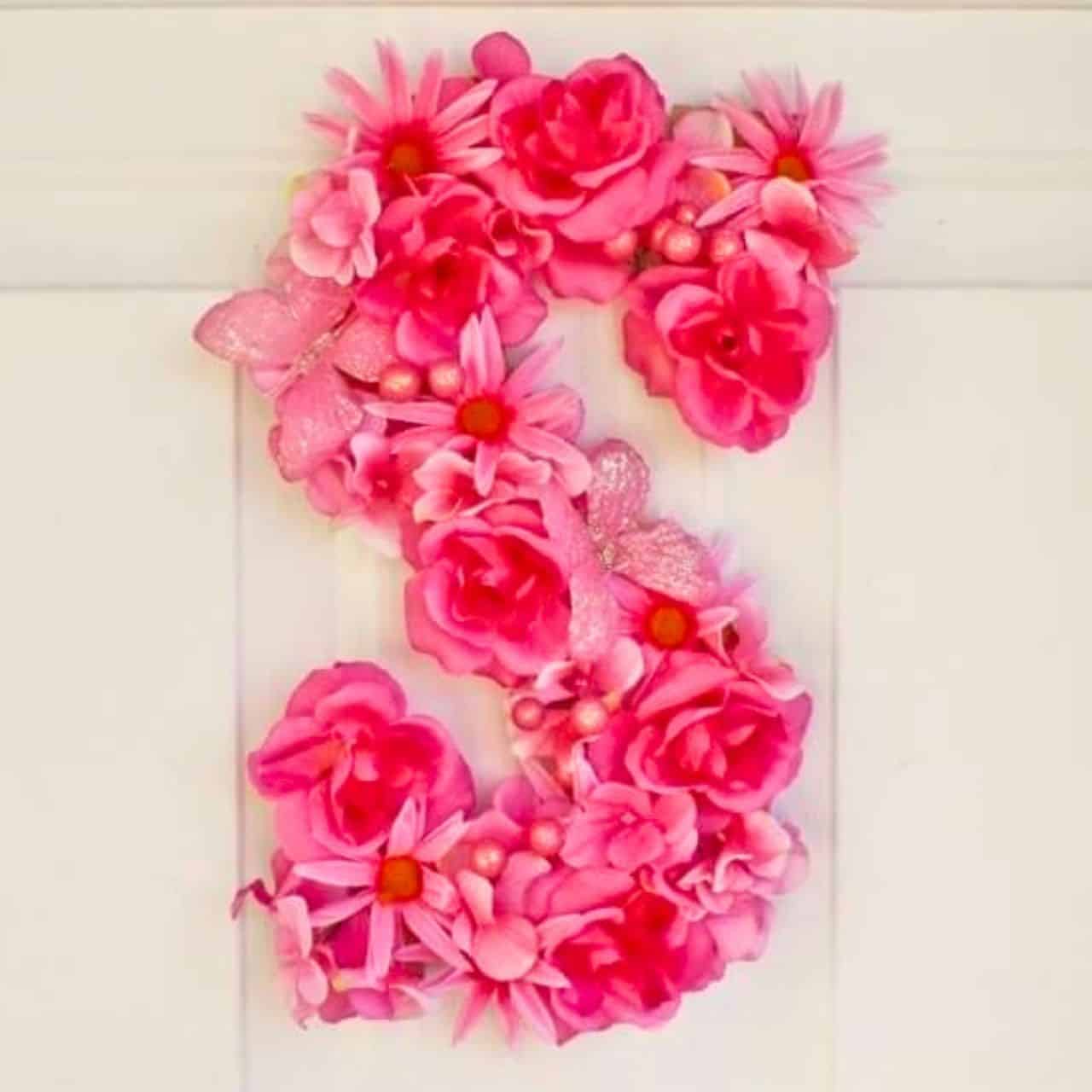 Pink floral letter E door hanging decorated with roses, daisies, butterflies, and pearl accents on a white door.