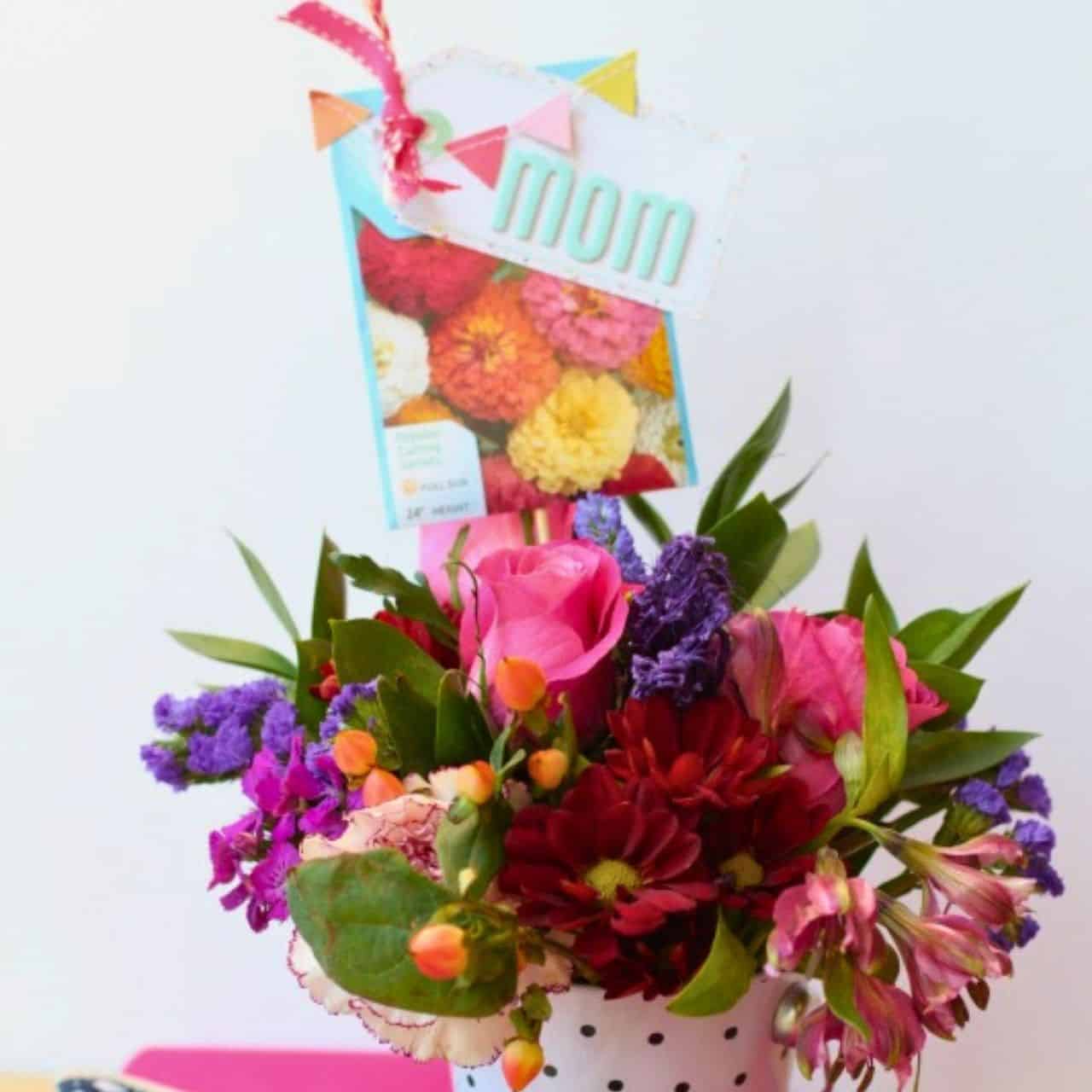 Colorful Mother's Day flower arrangement in a white pot with a handmade mom tag and seed packet decoration.