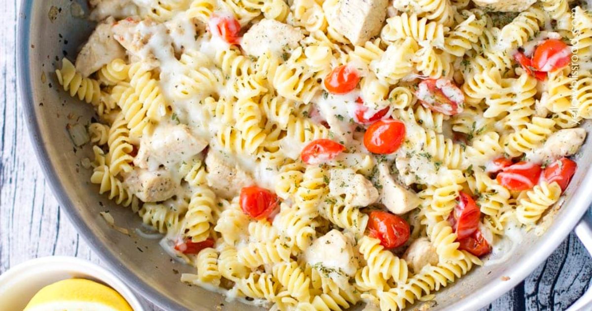 Skillet of rotini pasta with diced chicken, cherry tomatoes, and creamy sauce, lightly seasoned with herbs and mixed together.