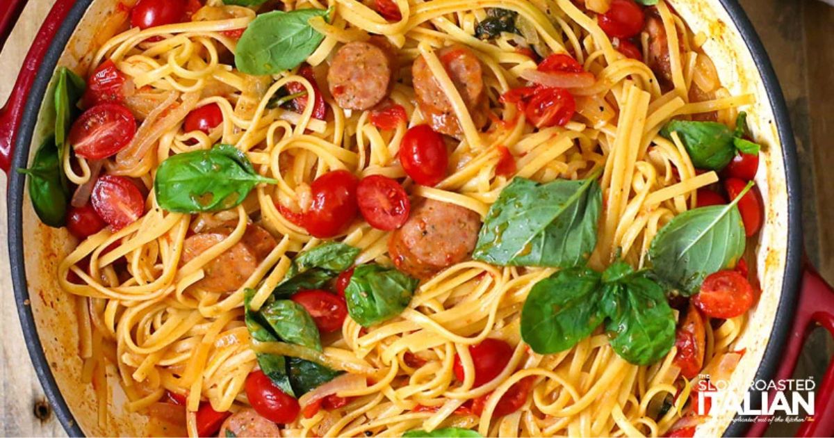 Skillet of spaghetti with sliced sausage, cherry tomatoes, onions, and fresh basil tossed together in a light sauce.