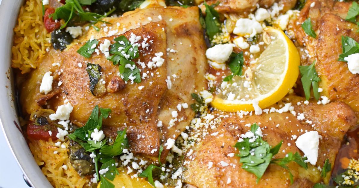 Chicken pieces on rice topped with crumbled cheese, lemon slices, and chopped herbs in a one pot dish.