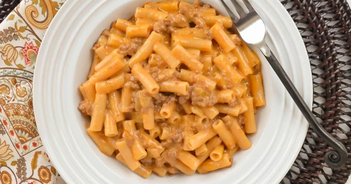 Bowl of creamy pasta with ground meat and cheese sauce, served with a fork on a patterned placemat.