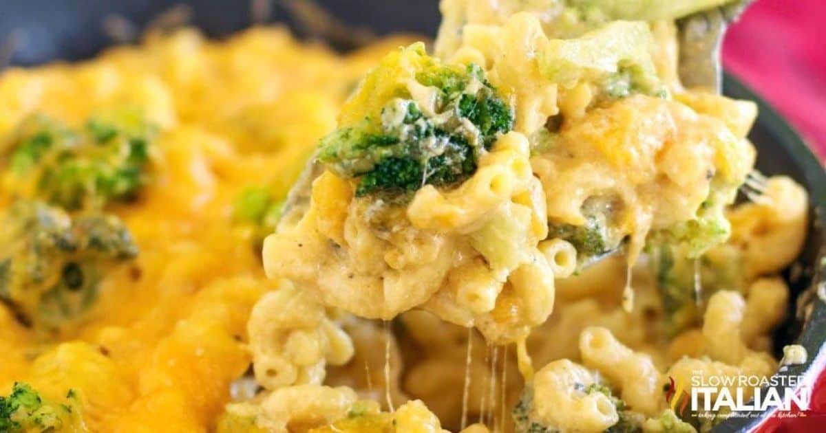 Spoon lifting creamy macaroni and cheese with broccoli from a skillet, showing melted cheese stretching between the pasta.