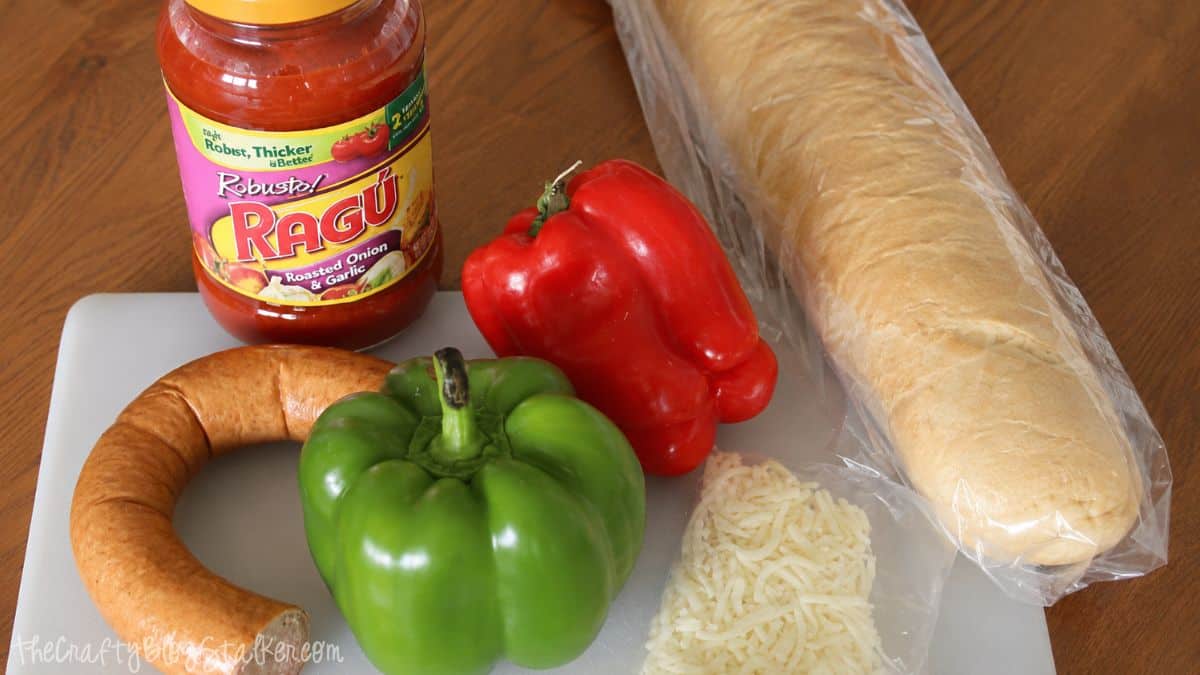 Ingredients for sausage bruschetta including Italian sausage, red and green bell peppers, mozzarella cheese, pasta sauce, and French bread.