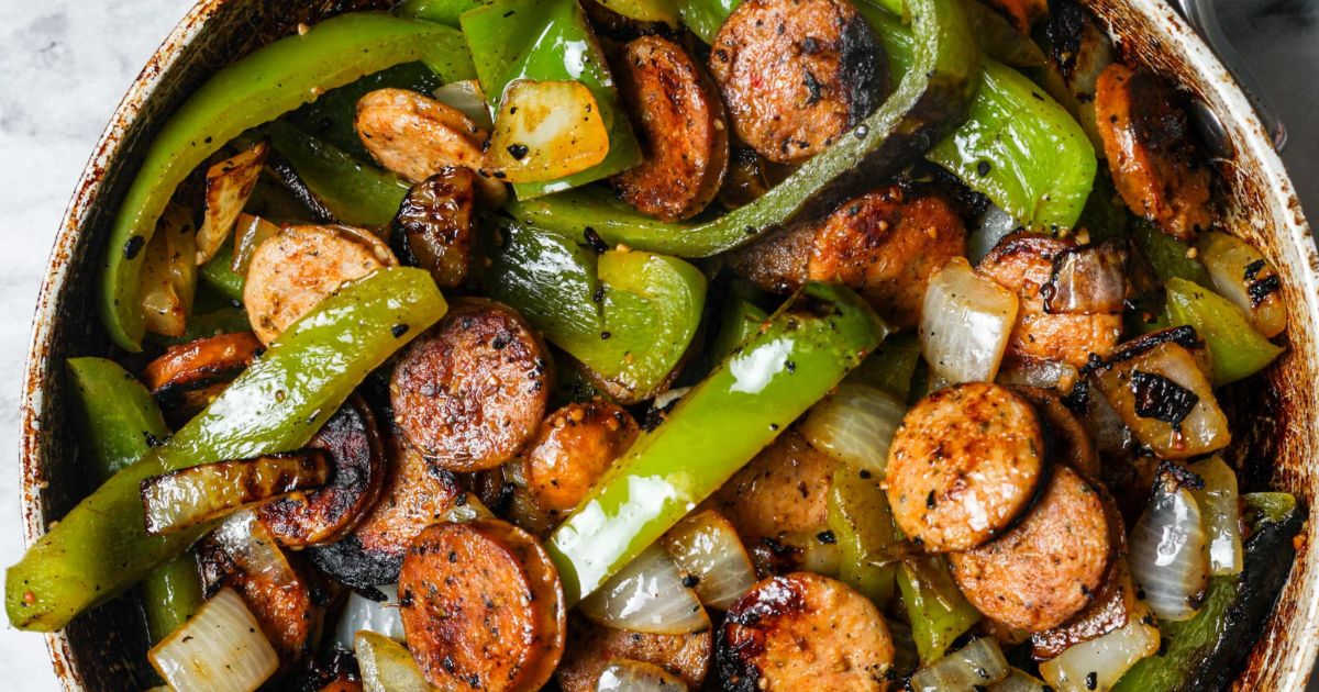 Skillet with sliced sausage, green bell peppers, onions, and mushrooms sautéed together with browned edges and seasoning.