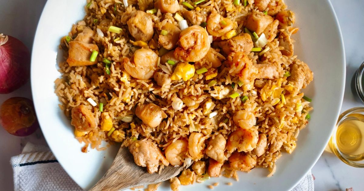 Plate of fried rice with shrimp, chicken, eggs, and green onions, mixed together and served with a wooden spoon.