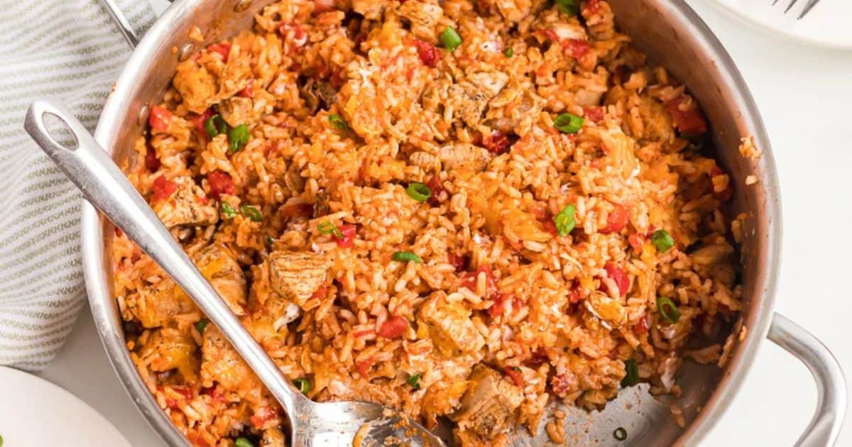 Skillet filled with seasoned rice, diced chicken, tomatoes, and green onions, mixed together and served with a spoon.