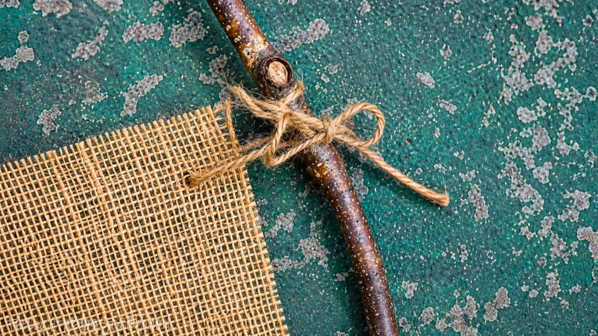 Close-up of burlap fabric tied to a small tree branch with twine for a rustic handmade flower holder project.