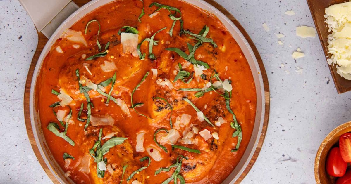 Chicken pieces in a creamy tomato sauce topped with fresh basil and shaved cheese, served in a shallow dish.