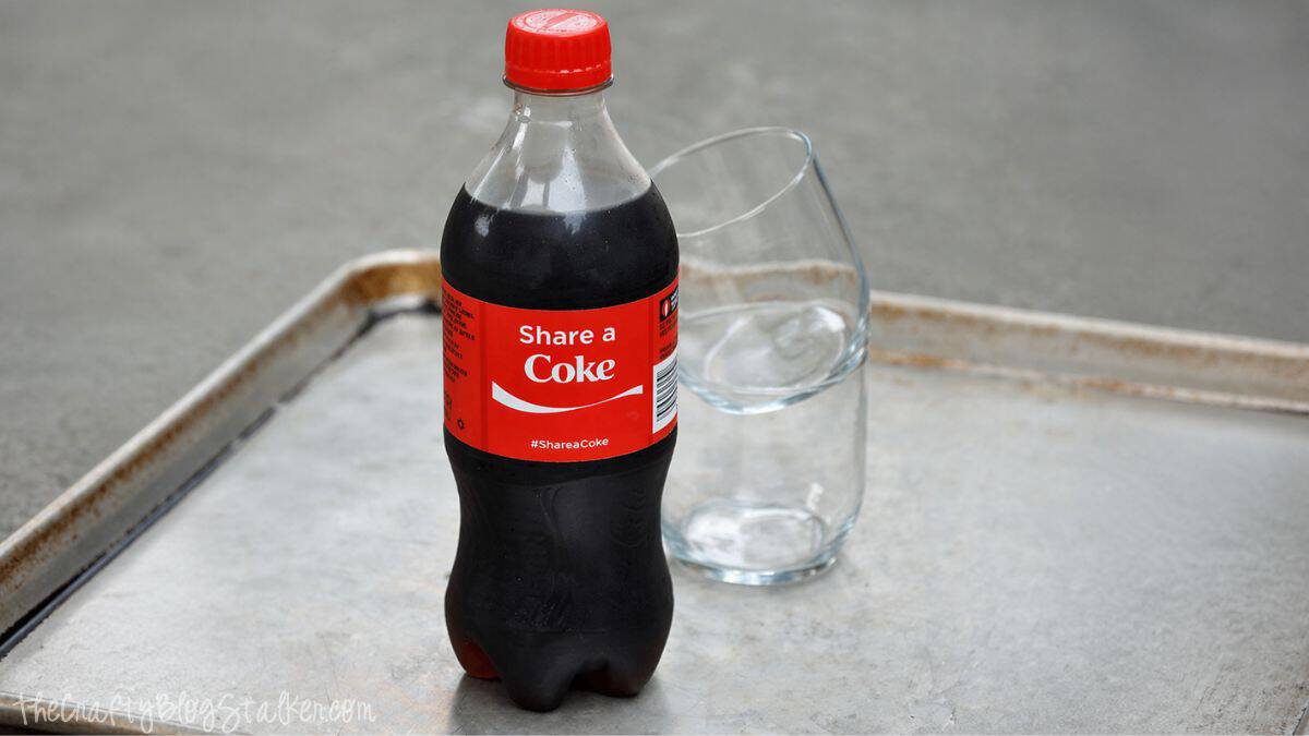 Bottle of Coca-Cola with a red cap next to an empty glass on a metal tray.