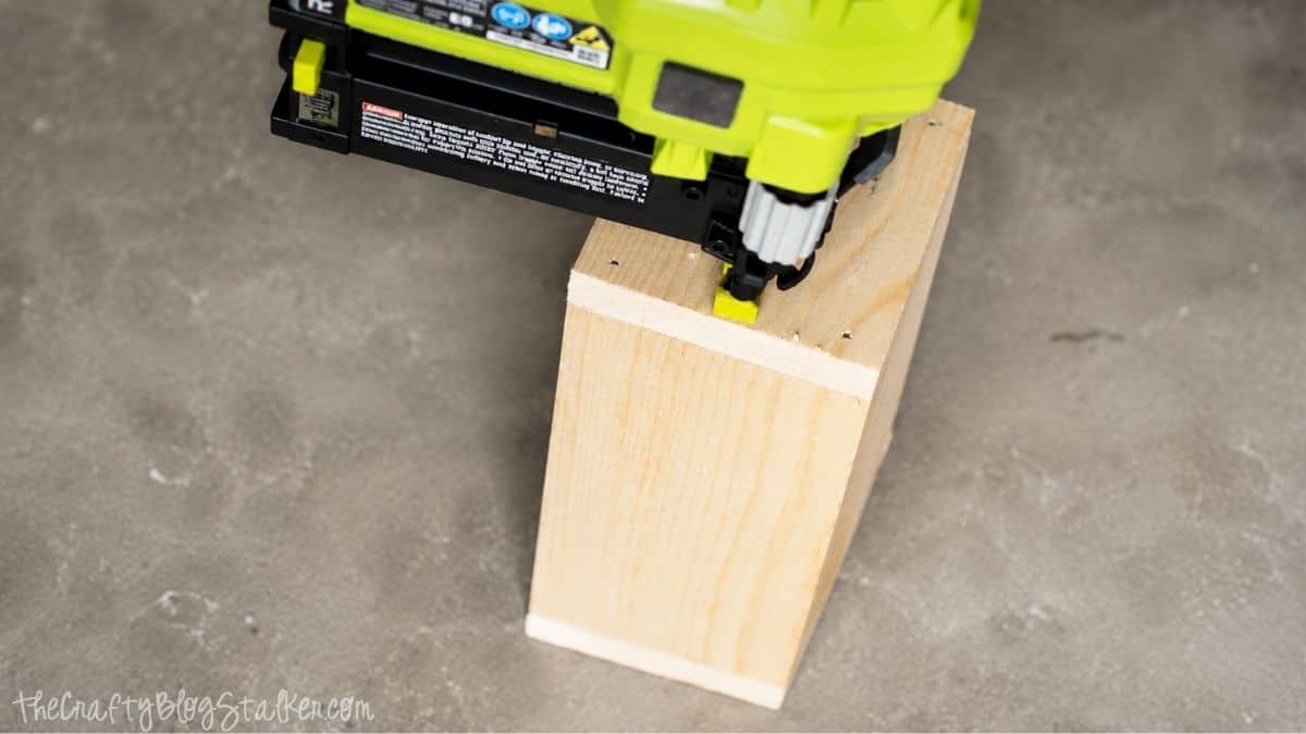 Make your very own Chalkboard Candle Box complete with DIY Citronella Candles Close-up of a brad nailer fastening an unfinished wooden box together during the assembly of a DIY citronella candle holder.