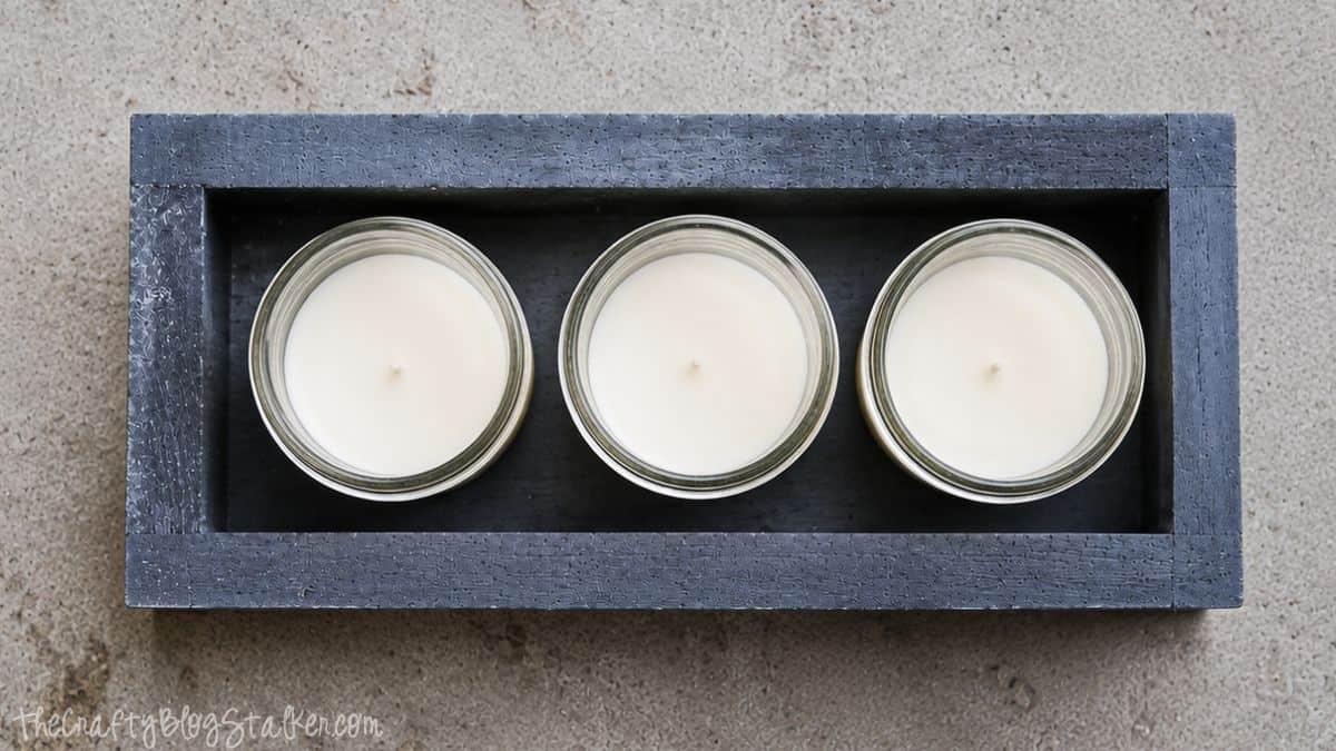 Make your very own Chalkboard Candle Box complete with DIY Citronella Candles Top view of a black painted wooden box holding three mason jar citronella candles, creating a simple DIY outdoor centerpiece.