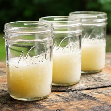 Three finished homemade citronella candles in glass mason jars on an outdoor table, ready to add soft light and help repel mosquitoes.
