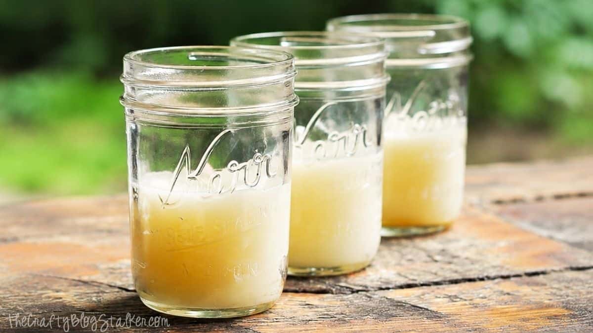 Drie stenen potten gevuld met gesmolten citronella-kaarsvet, afkoelen op een rustieke buitentafel voordat de kaarsen volledig uitharden.