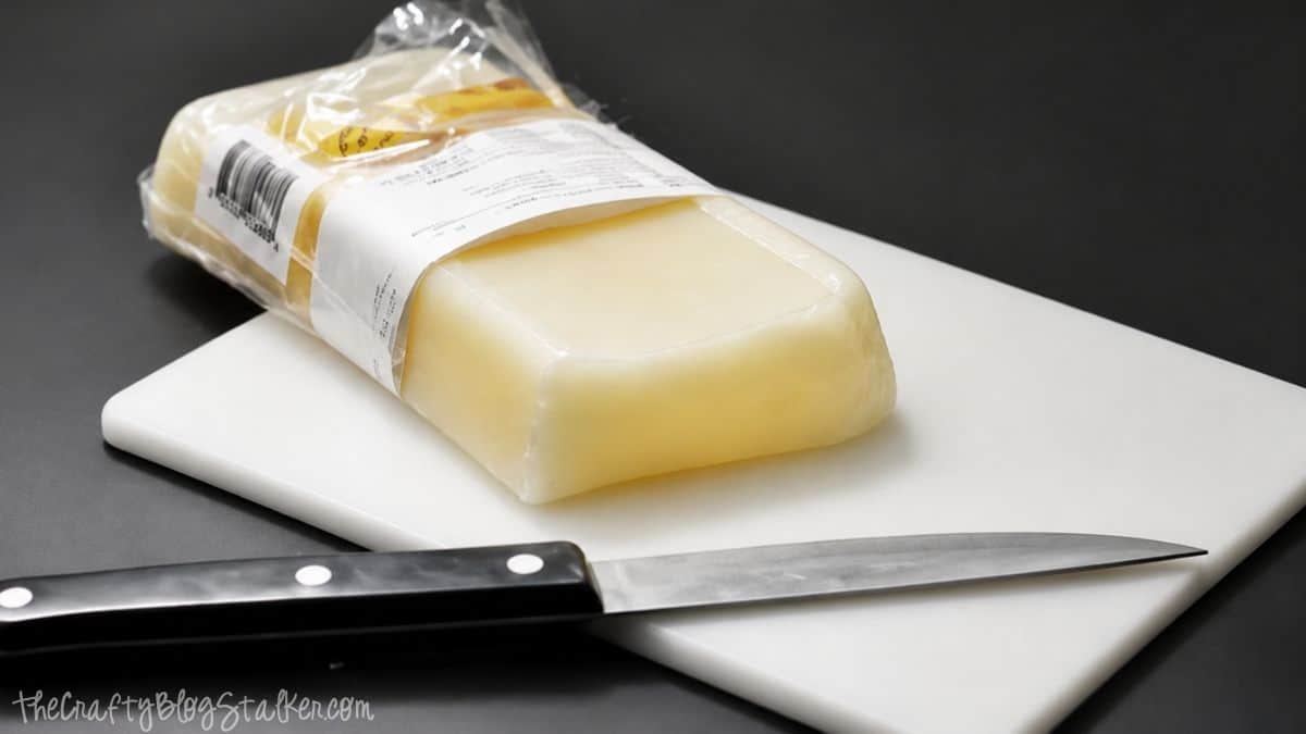 Blokje bijenwas op een snijplank met een mes, klaar om in kleinere stukjes te worden gesneden voor het maken van zelfgemaakte citronellakaarsen.