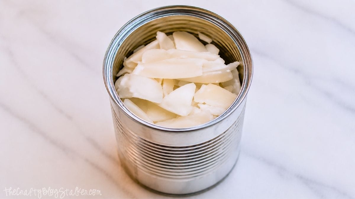 Metalen kaarsenblik gevuld met stukjes bijenwas, klaar om te worden gesmolten voor het maken van zelfgemaakte citronellakaarsen.