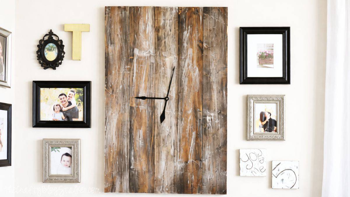 Large rustic wall clock made from weathered wood planks, mounted on a gallery wall surrounded by framed family photos and decorative accents.