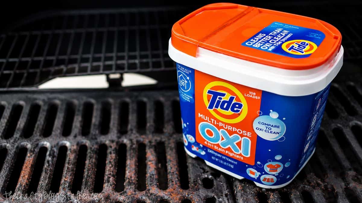 Do you have a gross grill? Learn How to Clean your BBQ Grill fast and easy! Container of Tide Oxi cleaner sitting on dirty barbecue grill grates before cleaning outdoors.