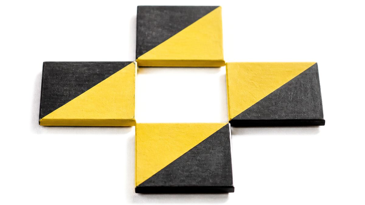 Four square coasters painted in yellow and black diagonal blocks arranged in a cross pattern with a small empty square space in the center.