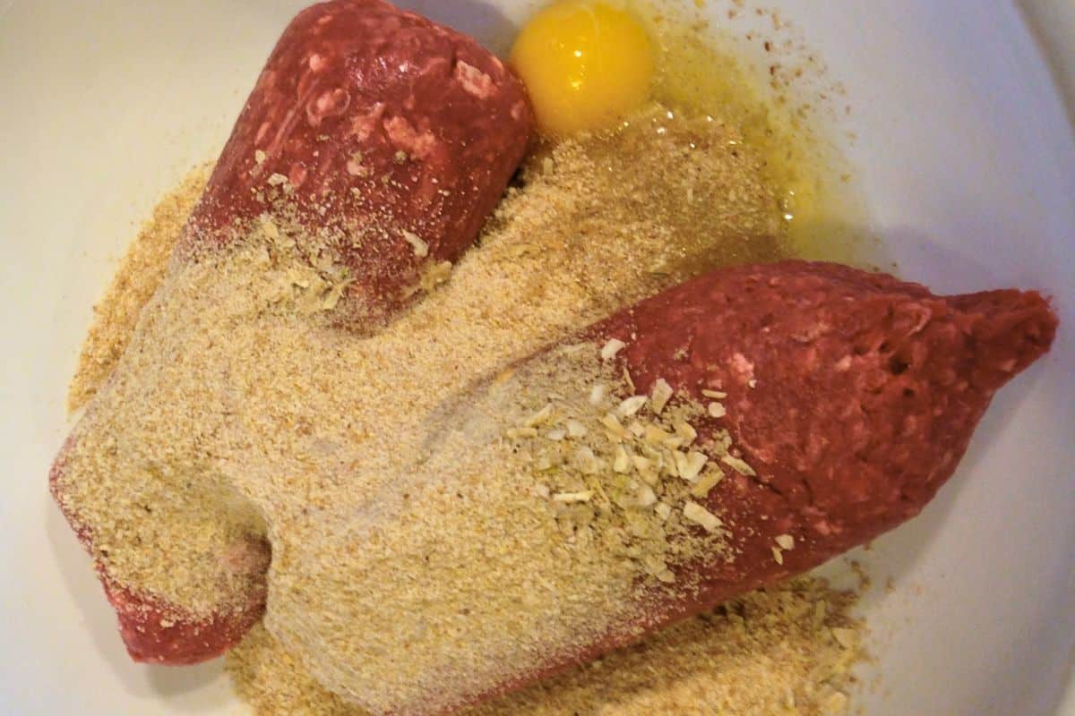 A bowl with ground beef, bread crumbs, and a cracked egg.