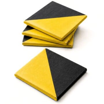 Stack of square coasters with a diagonal yellow and black design, with one coaster displayed in front on a white background.