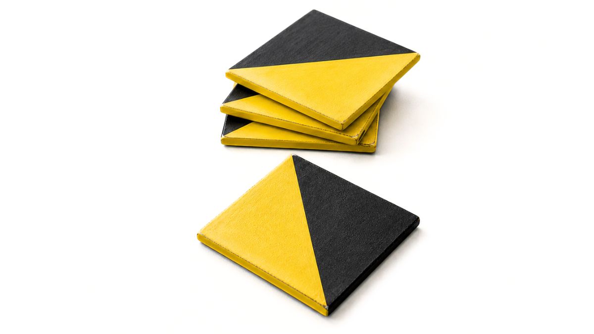 Stack of square coasters painted in a diagonal yellow and black color block design, with one coaster placed in front on a white background.