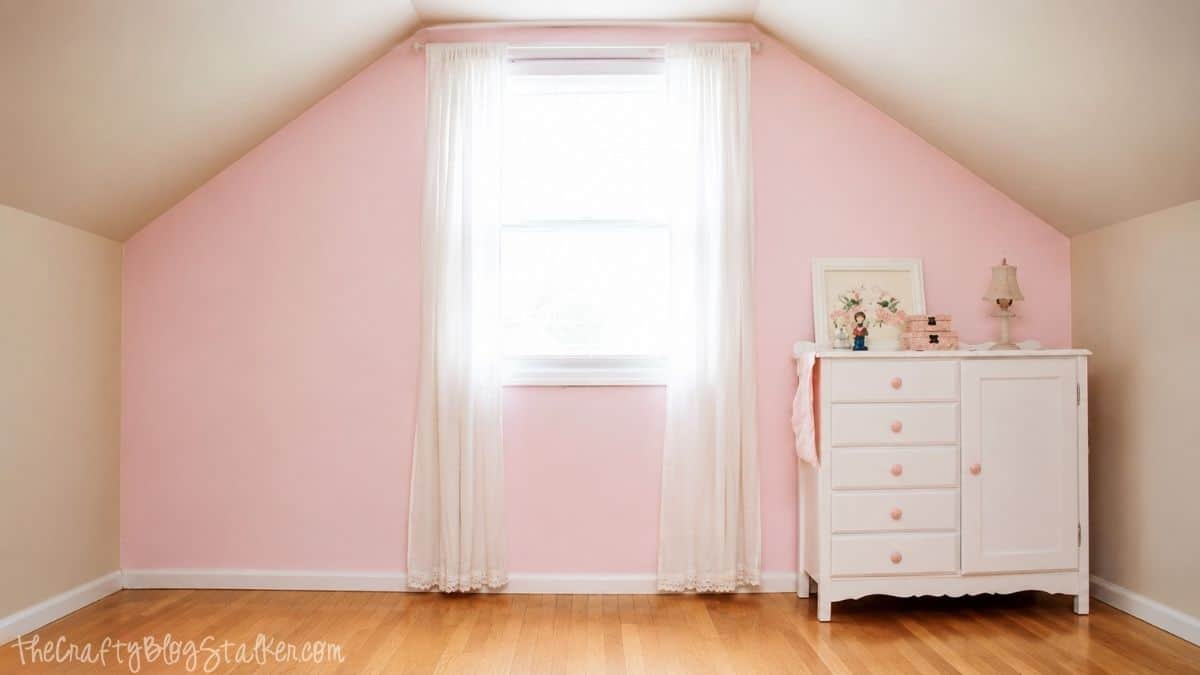 A Pink Shabby Chic Accent wall | Perfect for any little girl! Finished bedroom with a soft pink accent wall, tall window with white curtains, hardwood floors, and a white vintage dresser.
