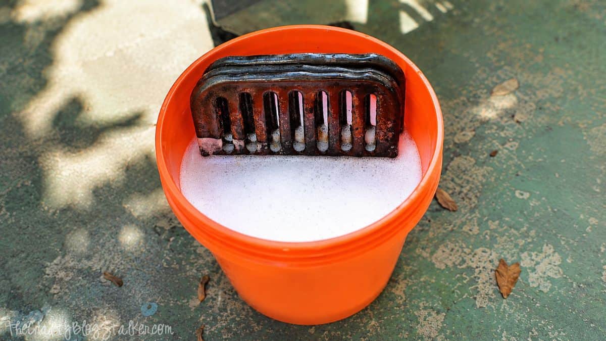 Do you have a gross grill? Learn How to Clean your BBQ Grill fast and easy! Dirty grill grates soaking in soapy water inside an orange bucket during an outdoor BBQ grill cleaning process.