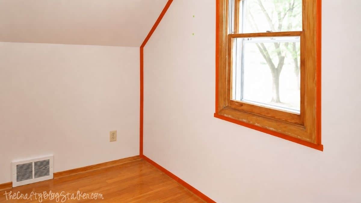 A Pink Shabby Chic Accent wall | Perfect for any little girl! Orange painter's tape outlines the window, baseboards, and edges of a white accent wall before painting.