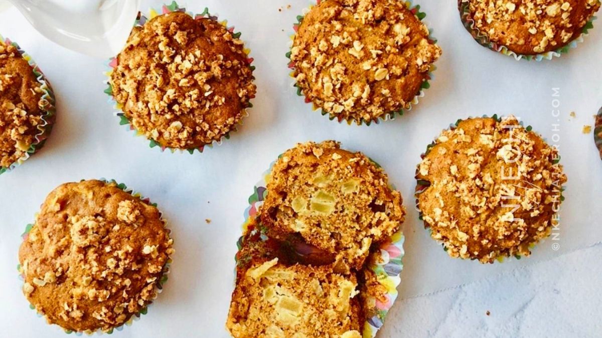 Freshly baked apple crumble muffins topped with oat streusel, with one muffin cut open to show chunks of apple inside.