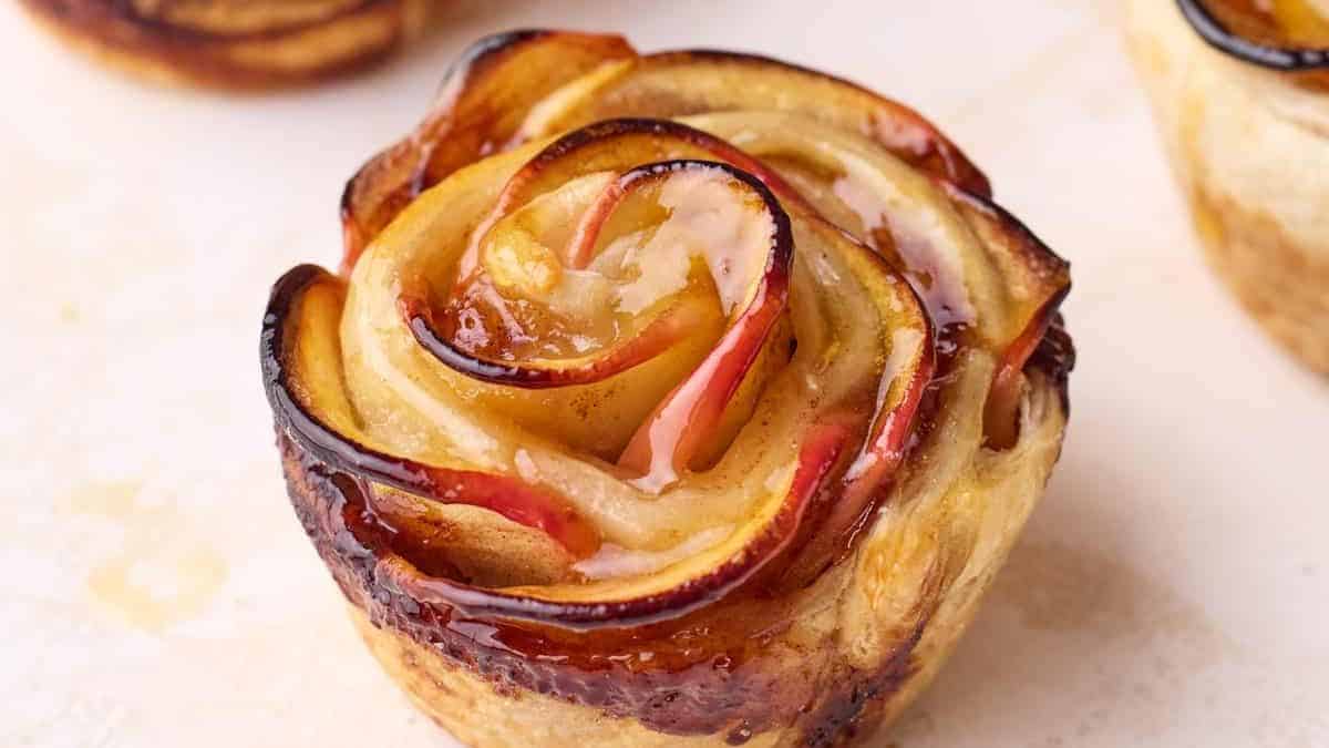 Close-up of a baked apple rose pastry with thin apple slices shaped like petals and a glossy golden glaze.