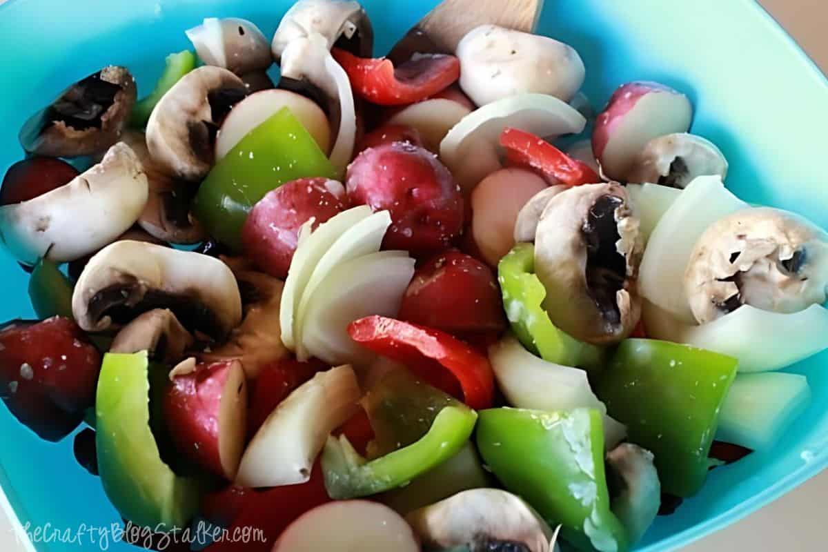 A blue bowl of washed and cut fresh vegetables; mushrooms, onion, green pepper, and red pepper.