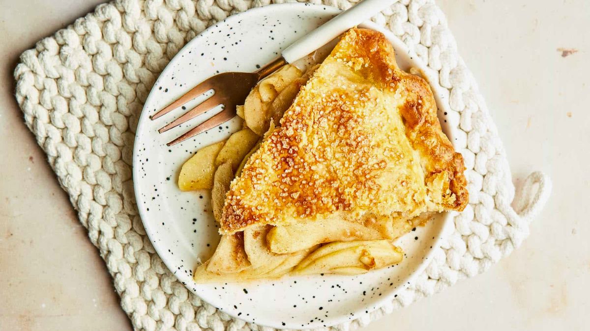 Slice of Granny Smith apple pie with golden flaky crust and sugar topping on a white plate with a fork.