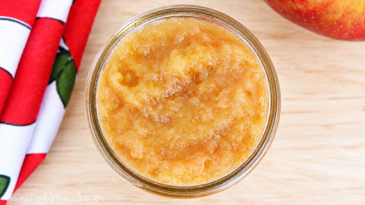 Close-up of homemade applesauce in a glass jar on a wooden surface.