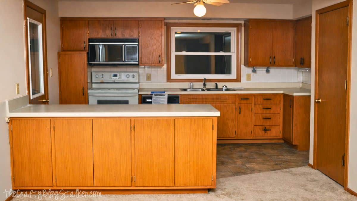 Older kitchen with wood cabinets, white appliances, laminate countertops, and an island before a farmhouse-style kitchen makeover.